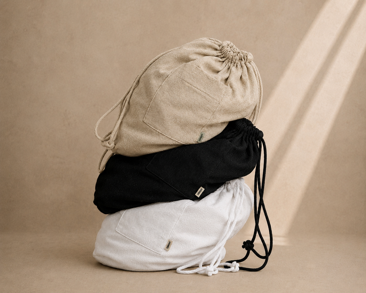 Three drawstring storage bags stacked on top of each other in beige, black, and white, set against a warm beige background with soft diagonal shadows. Hemp Horizon