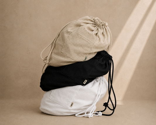 Three drawstring storage bags stacked on top of each other in beige, black, and white, set against a warm beige background with soft diagonal shadows. Hemp Horizon