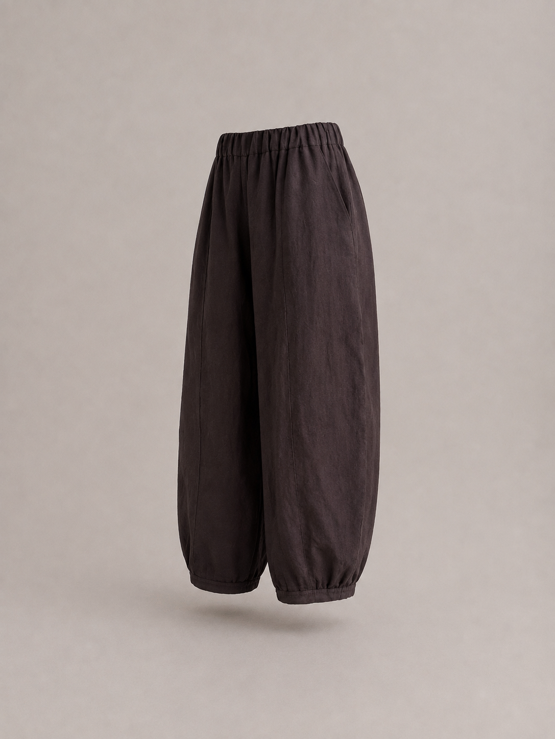 Dark brown baggy pants with an elastic waistband and gathered cuffs, shown floating against a neutral gray background. emp Horizon