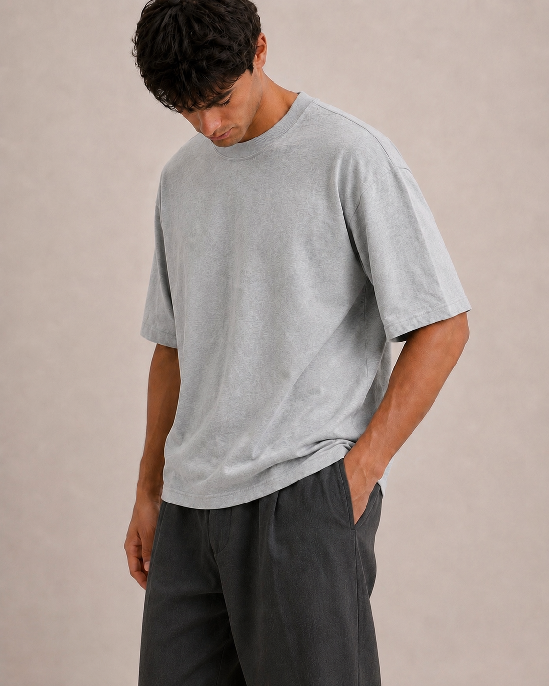 A man wearing a light gray oversized t-shirt and dark gray trousers, standing against a neutral beige background. Hemp Horizon