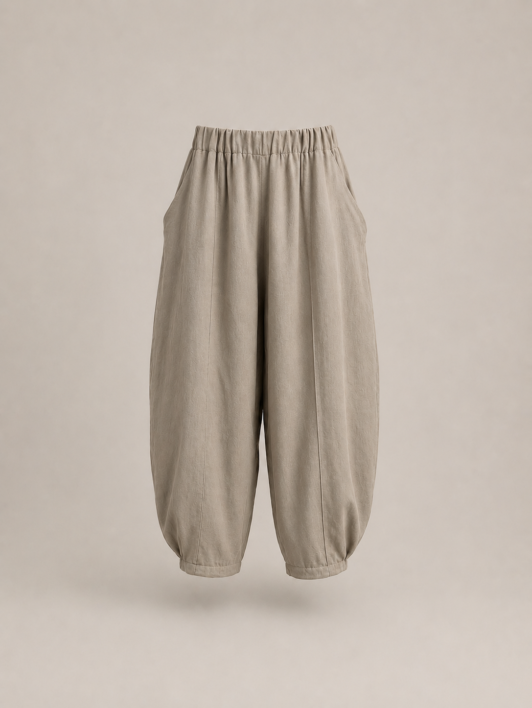 A pair of loose, balloon-style pants in a light taupe-beige fabric, featuring an elastic waistband and gathered cuffs, shown against a solid neutral beige background. Hemp Horizon
