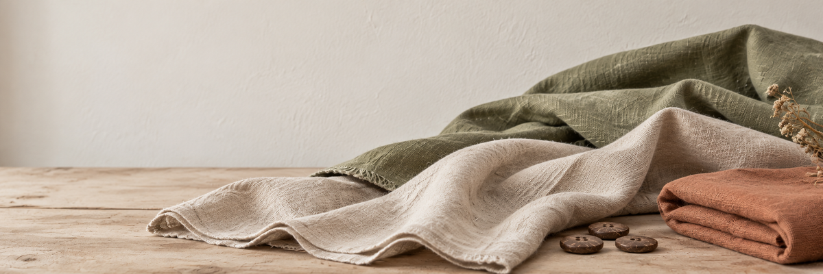 Natural cream, olive and terracotta fabrics with coconut buttons on a pale wooden table.